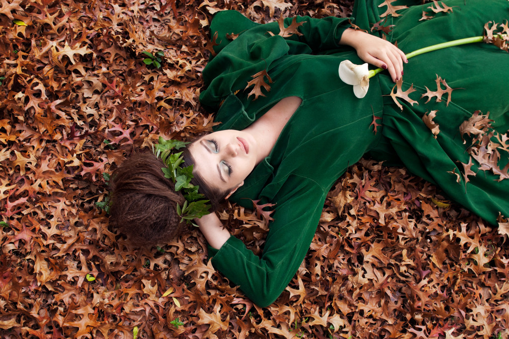 Sleeping Beauty wearing a green dress asleep in autumn leaves