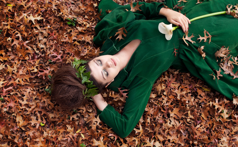 Sleeping Beauty wearing a green dress asleep in autumn leaves
